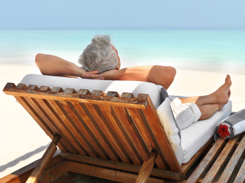 Rear view of mature guy relaxing on deck chair at the beach