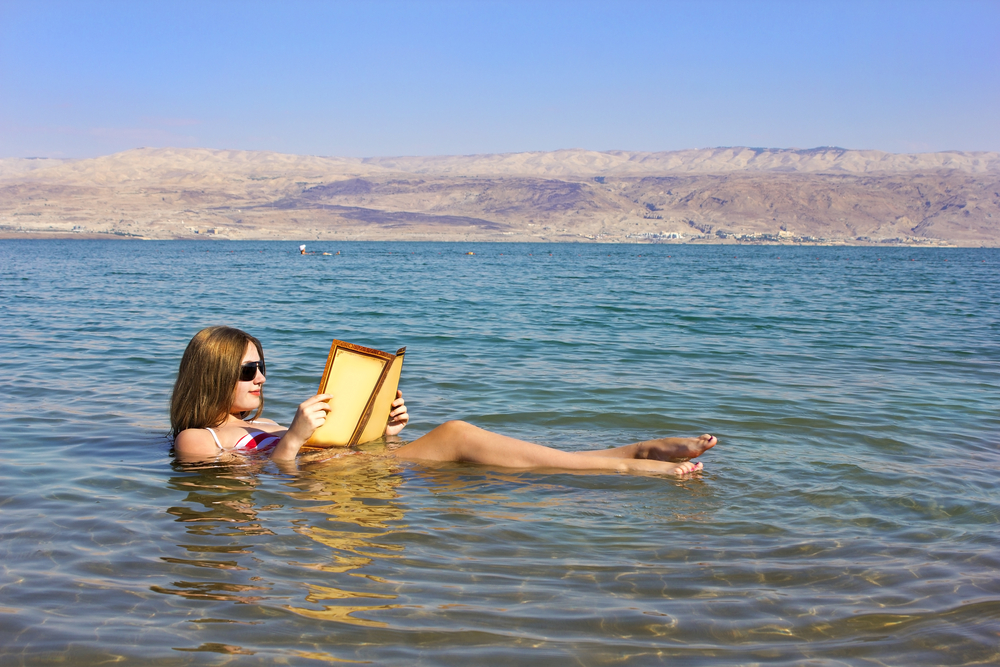 Woman reading a book while floating in the Dead Sea, Israel. 