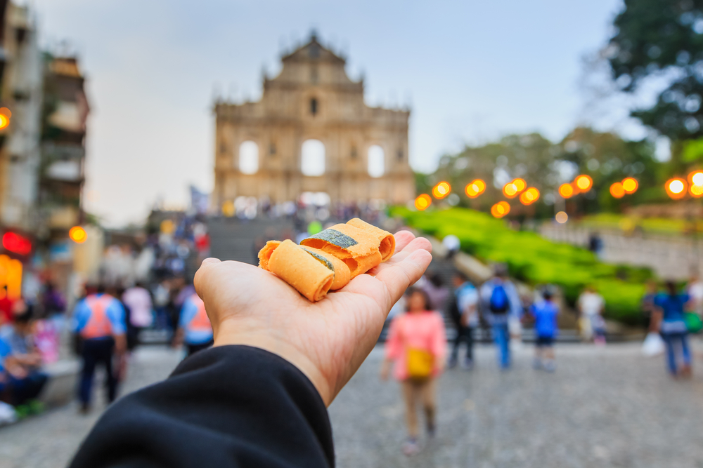 Man holding up snacks with Macau as background